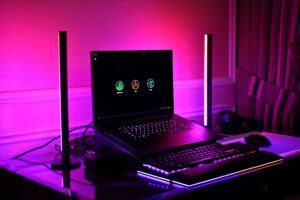 Laptop de gaming așezat pe un cooler RGB iluminat cu albastru și mov într-un setup modern
